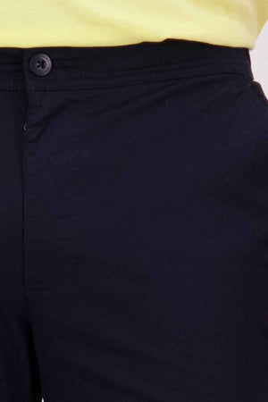 Close-up of a person wearing the Swanndri Sandy Point Short, stylish black shorts featuring a button and zipper, designed with multiple pockets, paired perfectly with a yellow shirt at the waist.