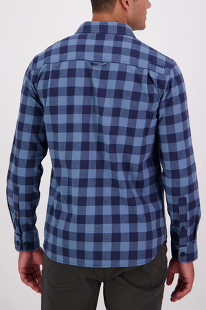 A person stands facing away, showcasing the back of the blue and navy check Swanndri Taranaki Tailor Shirt—100% cotton with buttoned chest pockets—against a plain light background.