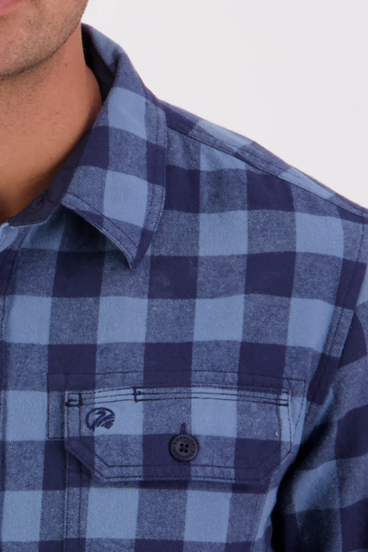 Close-up of a person wearing the Swanndri Taranaki Tailor Shirt in blue and navy check cotton with buttoned chest pockets. The collar, shoulder, and part of the chest are visible; face is partially out of frame.