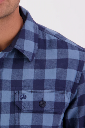 Close-up of a person wearing the Swanndri Taranaki Tailor Shirt in blue and navy check cotton with buttoned chest pockets. The collar, shoulder, and part of the chest are visible; face is partially out of frame.