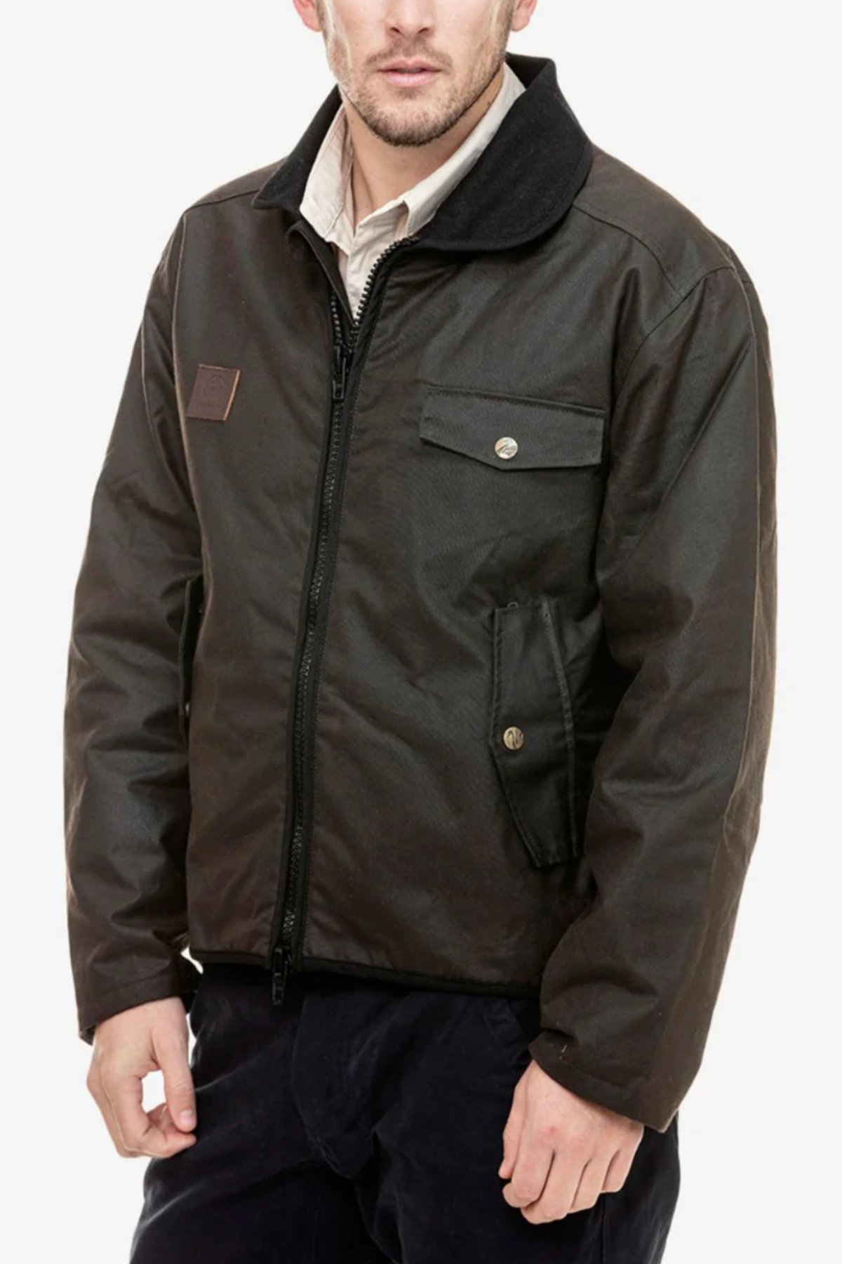 A man wears the Swanndri Waimak Oilskin Jacket, a dark brown waxed cotton zip-up with buttoned chest and side pockets, over a light collared shirt, standing against a plain white background.