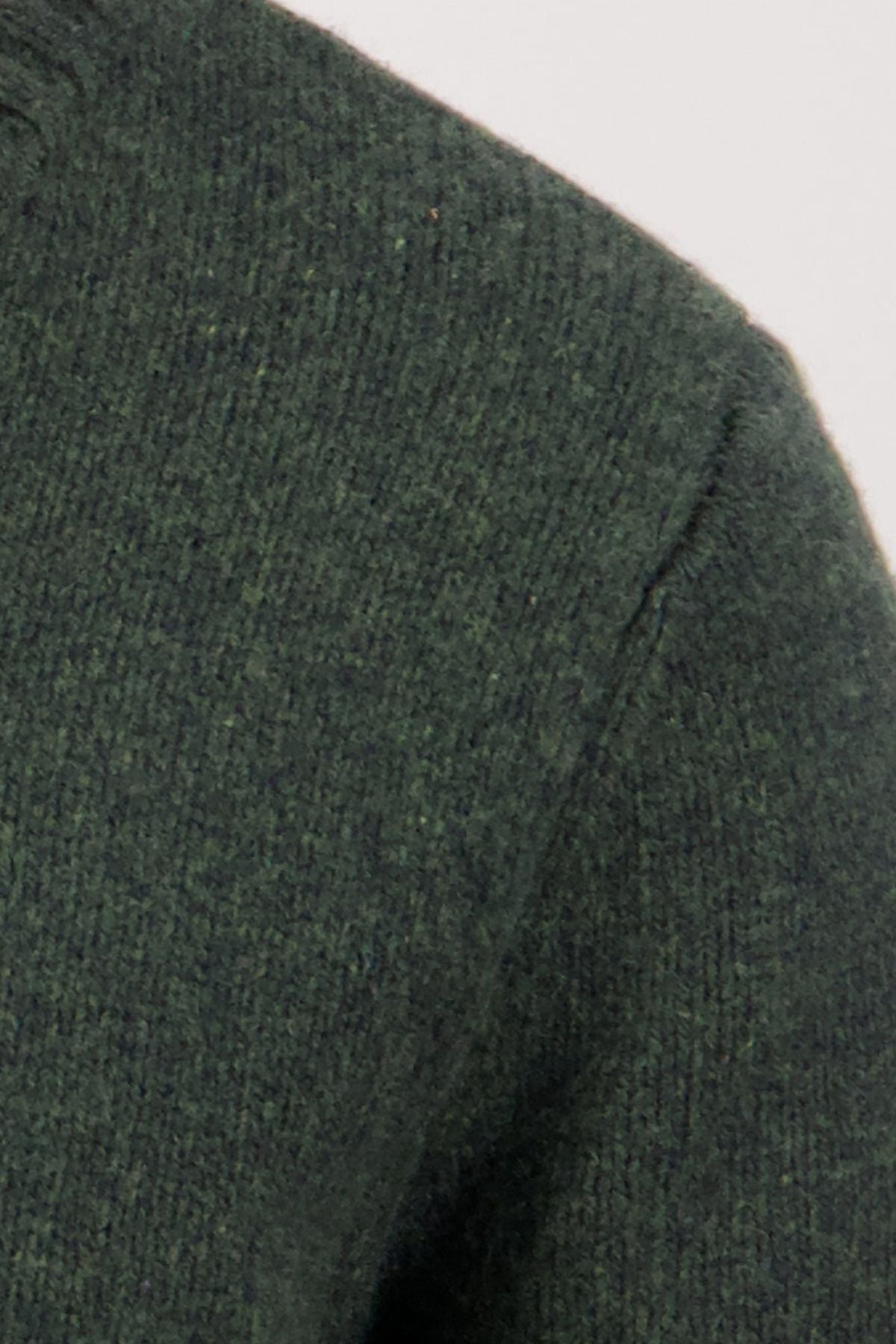 Close-up of the shoulder and sleeve of the Swaandri Waylins Wool Knit Crew in dark green, highlighting the textured stitching and durable wool knit against a plain light background.