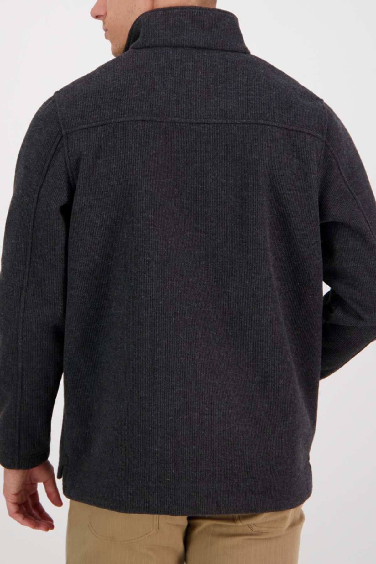 A man, shown from the back against a plain light background, wears the Swanndri Weka Sweater in dark gray with tan pants. His relaxed pose highlights the sweater’s breathable and windproof design.