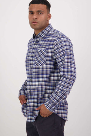 A man wearing a Swanndri Wendon Shirt, made from 100% cotton in classic fit, stands confidently against a plain background with his hands in his dark pants' pockets.