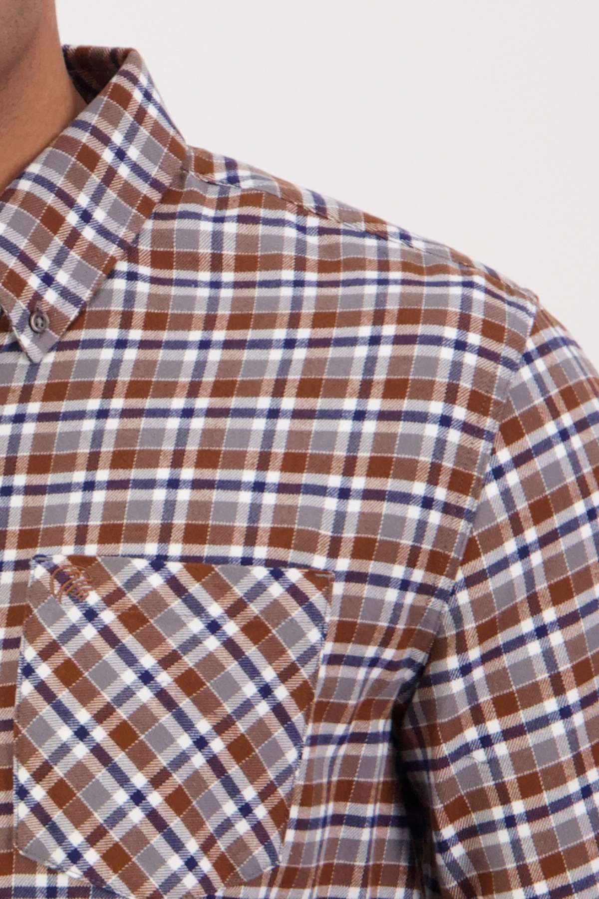 Close-up of a person wearing a Swanndri Wendon Shirt in a brown, blue, and white plaid pattern. The shot captures only the upper torso and part of the neck, highlighting the intricate pattern and texture of the 100% cotton fabric. This classic fit shirt is detailed with a front pocket.