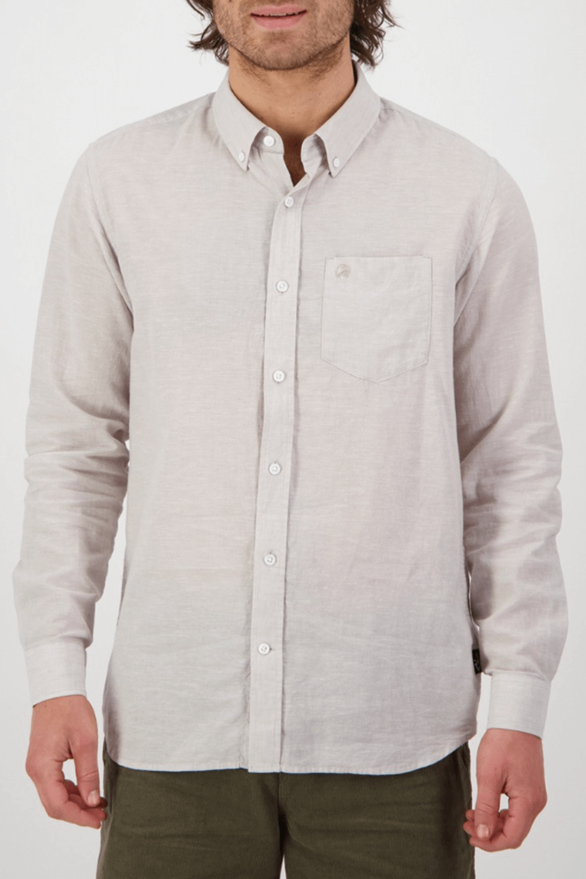 Wearing a tailored-fit Swanndri Wolcott v2 Long Sleeve Shirt with a classic collar and buttoned cuffs, crafted from a linen-cotton blend, a person pairs it with olive green pants against a plain white background.