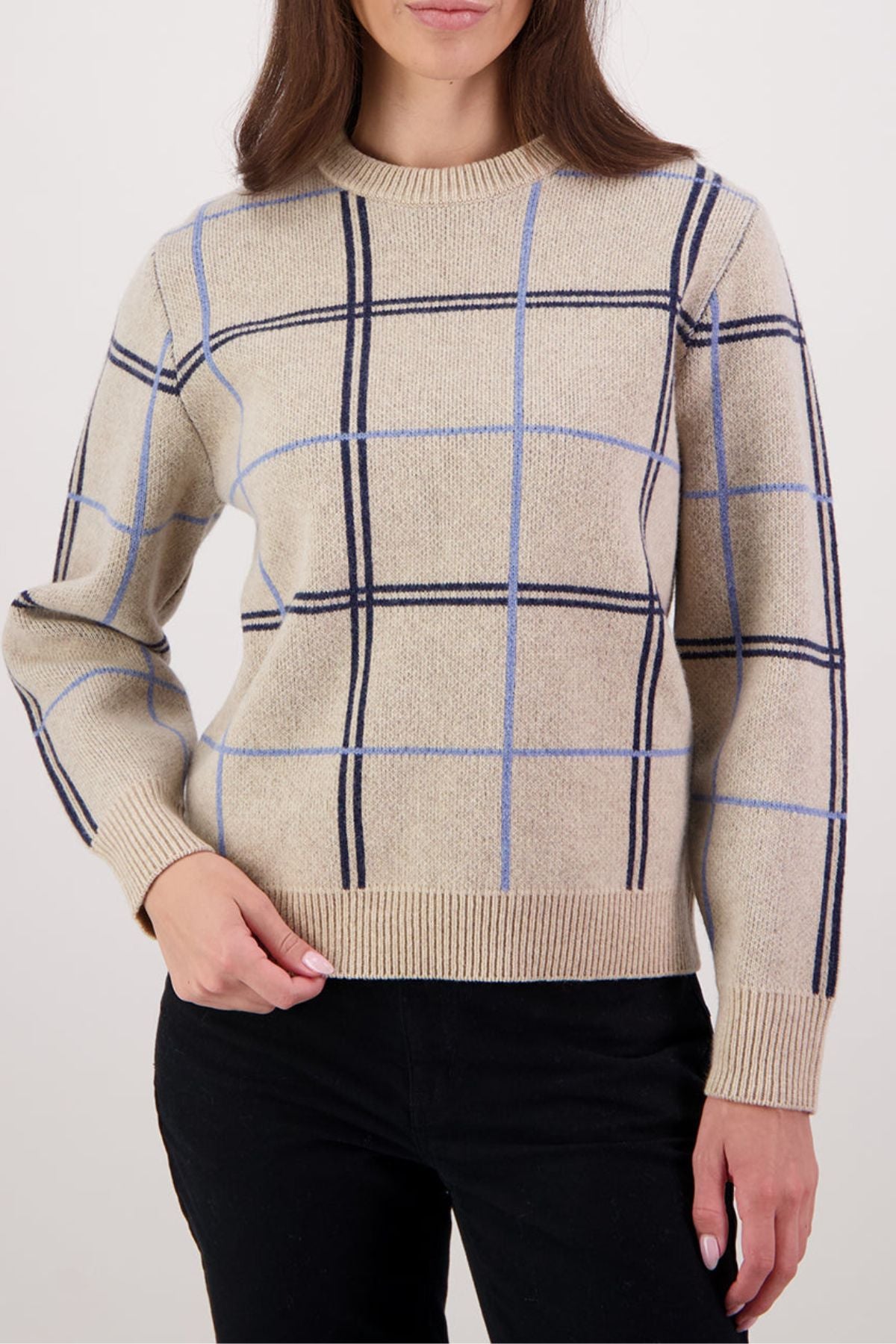 Wearing the Swanndri Yasmin Check Womens Knit in blue and black with black pants, a person stands against a plain light backdrop, their head partially out of frame.