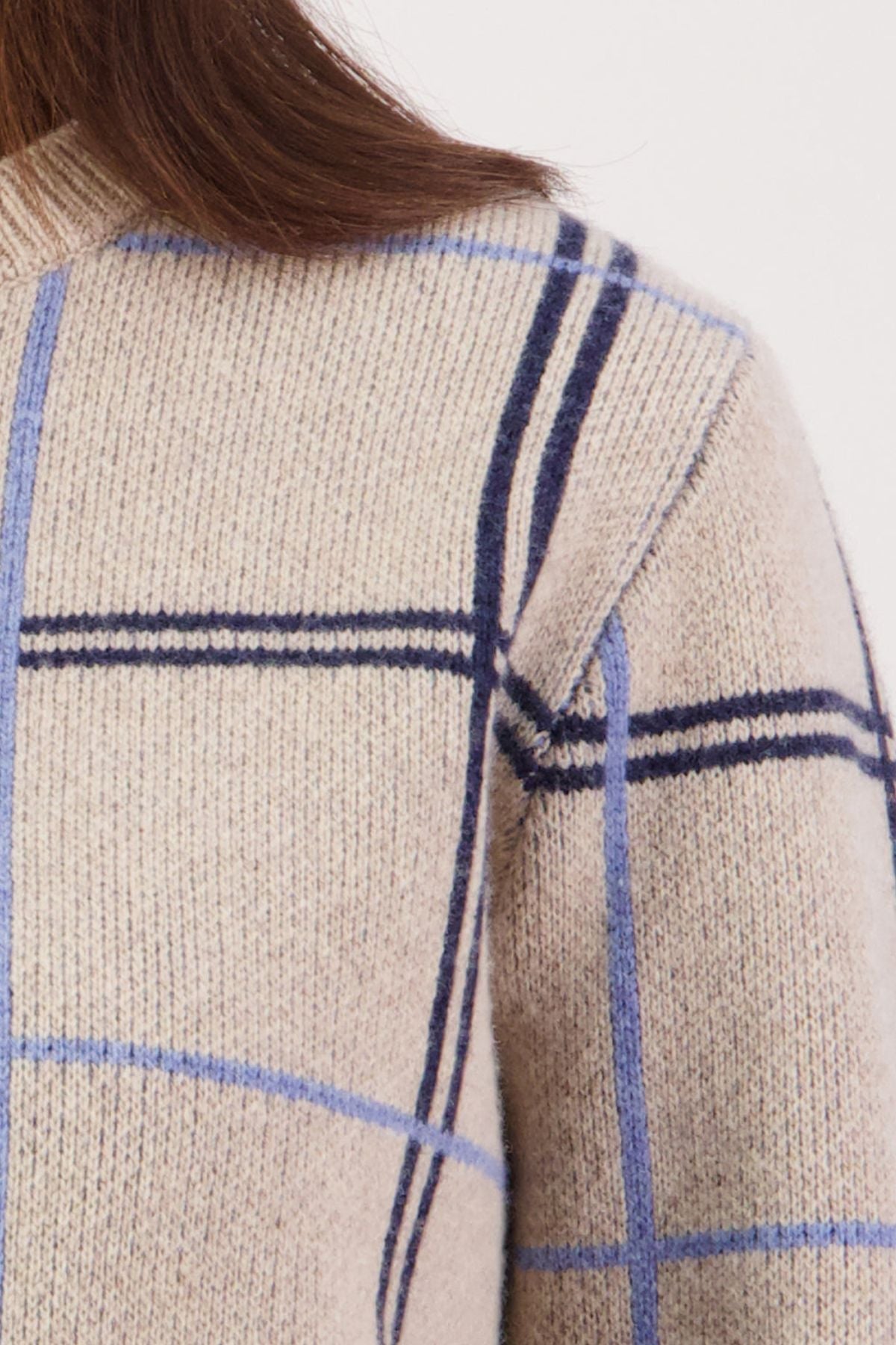 Close-up of the Swanndri Yasmin Check Womens Knit in beige merino wool with blue and navy plaid. A portion of a woman's shoulder, upper arm, and brown hair is seen against a plain light background.