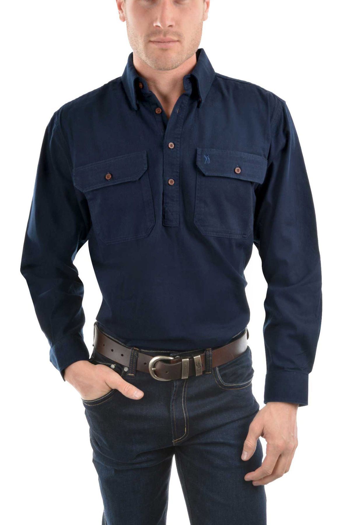 A man wears a dark blue Thomas Cook Heavy Drill Half Placket Shirt with two chest pockets, paired with dark jeans and a black belt, standing with one hand in his pocket against a white background.