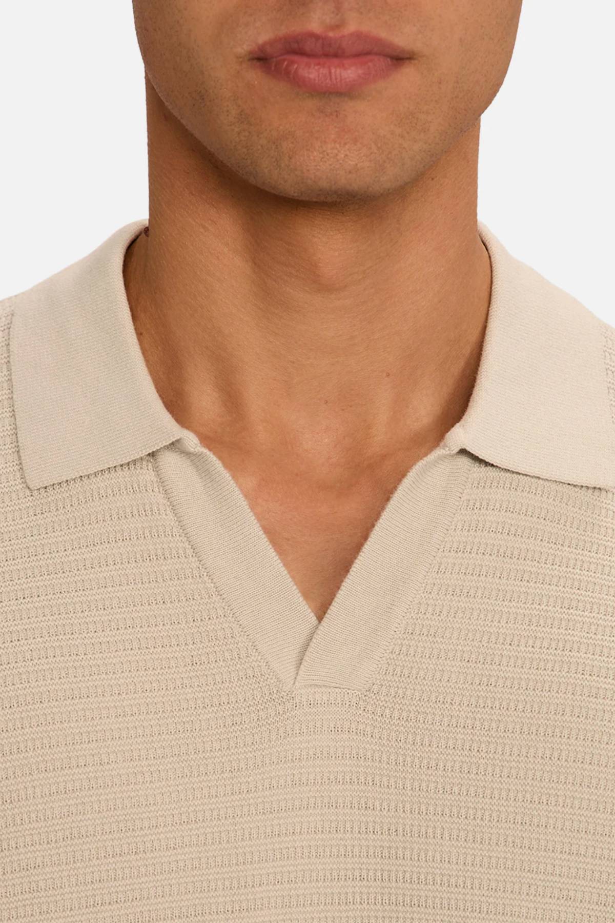 Close-up of a person wearing the Industrie The Alicante Polo in textured beige with a V-neck, showing the lower face, neck, and upper chest against a plain white background.