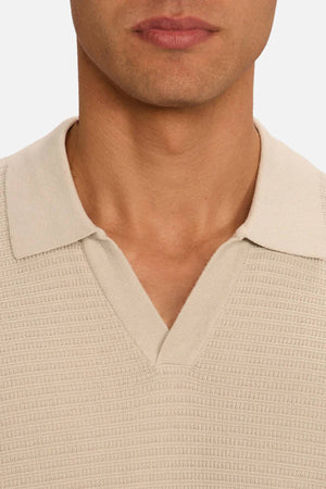 Close-up of a person wearing the Industrie The Alicante Polo in textured beige with a V-neck, showing the lower face, neck, and upper chest against a plain white background.
