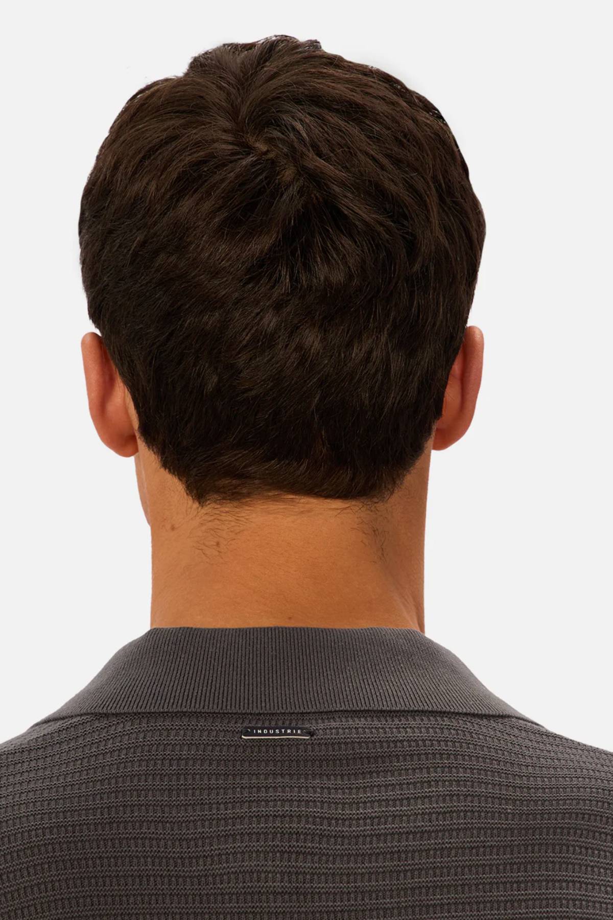 A man with short, dark brown hair is shown from behind, wearing the Industrie The Alicante Polo in textured dark gray against a plain light background.