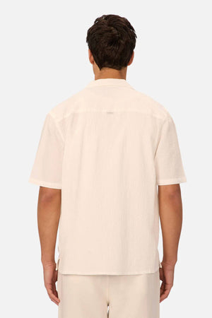 A man is seen from the back wearing the Industrie The Canyon Short Sleeve Shirt, a light-colored camp-collar short sleeve shirt, with matching pants against a plain light gray background.