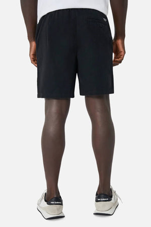 A person stands facing away in Industrie The Dublin Short—classic men's summer shorts—paired with white New Balance sneakers. The shorts have a right-side buttoned back pocket, shown against a plain white background.