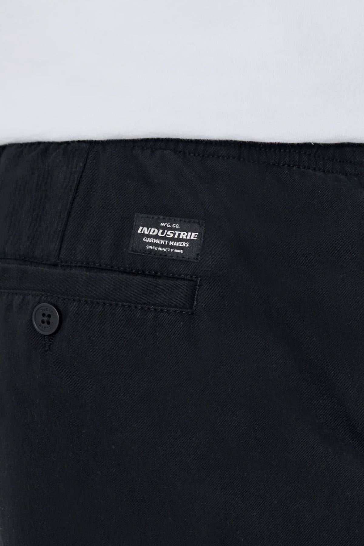 Close-up of the back of black Industrie The Dublin Short men’s summer shorts, featuring a buttoned pocket, a small rectangular "Industrie Garment Makers" label, and a white shirt tucked into the cotton-linen waistband.