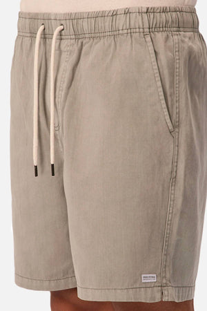 A close-up shows a person wearing Industrie The Dublin Short in light gray cotton-linen, featuring side pockets and a small rectangular label near the left hem—ideal men's summer shorts for comfort on warm days.