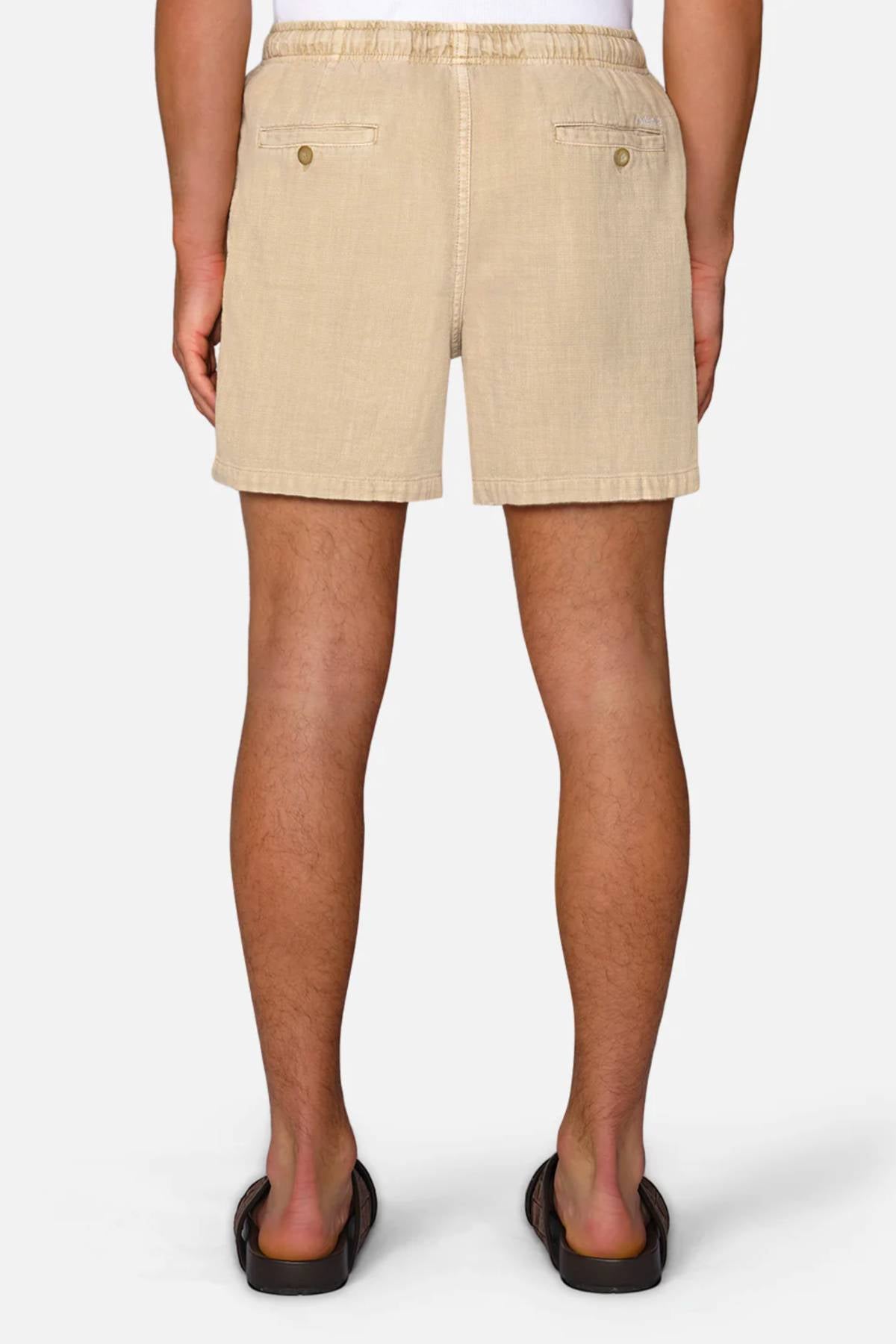 A person is shown from the back wearing Industrie The Mallorca Short, a men's cotton short with two buttoned back pockets, and black sandals, standing against a plain white background.