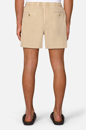A person is shown from the back wearing Industrie The Mallorca Short, a men's cotton short with two buttoned back pockets, and black sandals, standing against a plain white background.