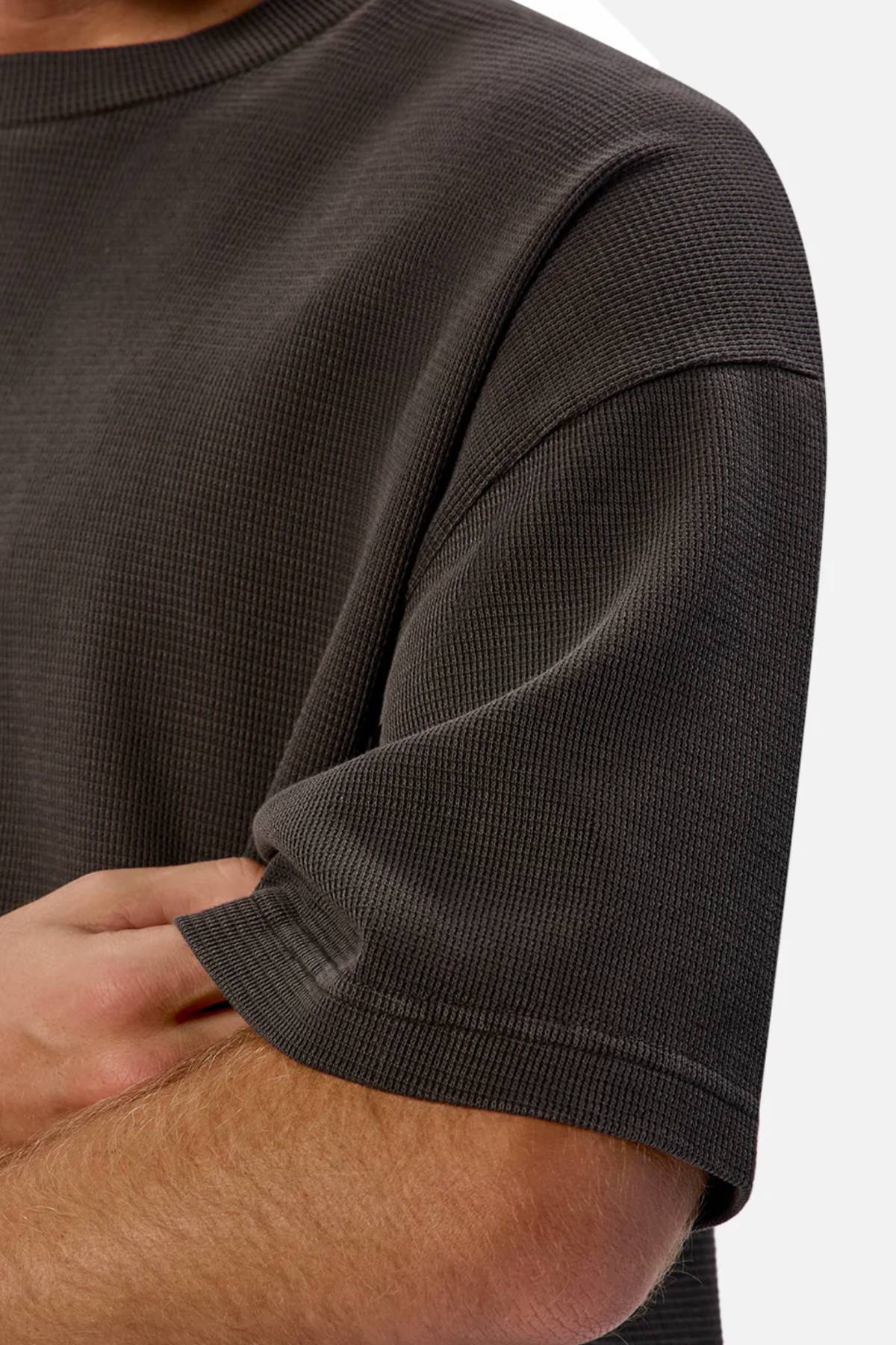 Close-up of a person’s arm and upper torso wearing Industrie The Marlon Tee, a textured dark gray T-shirt in a relaxed fit. Their other forearm is crossed beneath the sleeve, set against a neutral background.