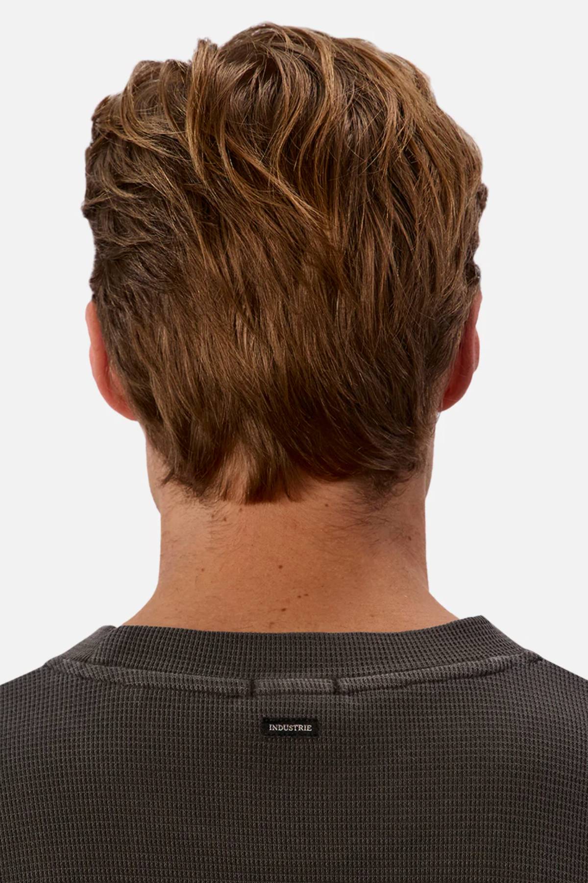 The image shows the back view of a person with short, wavy brown hair wearing a dark gray Industrie The Marlon Tee in relaxed fit waffle knit, with "INDUSTRIE" labeled at the neckline. The background is plain white.