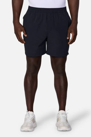A person is shown from the shoulders down against a plain background, wearing a white shirt, white sneakers, and Industrie The Owens Short—black quick-drying shorts with an elasticised waistband.