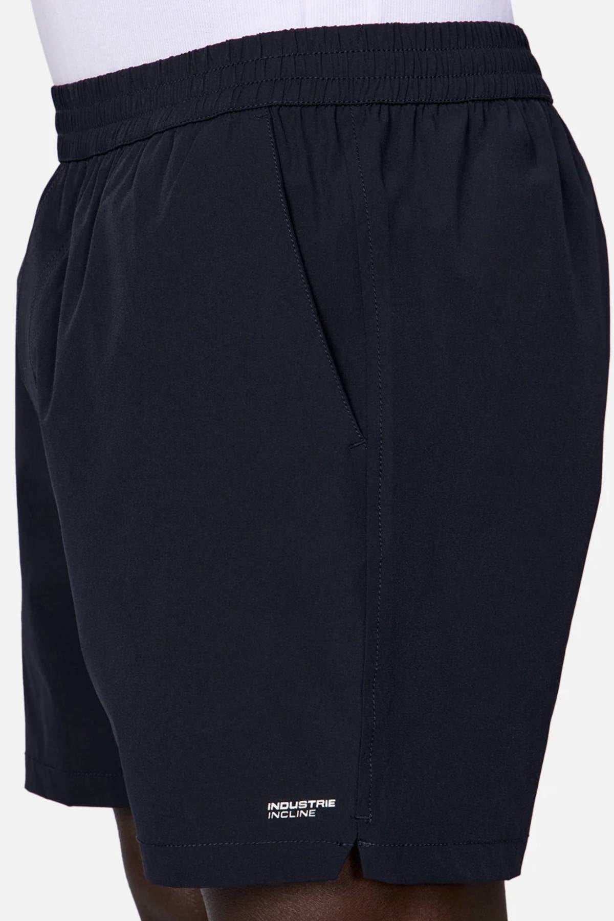 A close-up side view of a person wearing Industrie The Owens Short—black, quick-drying, above-knee shorts with an elastic waistband, side pockets, and a small white "INDUSTRIE INCLINE" logo near the hem.