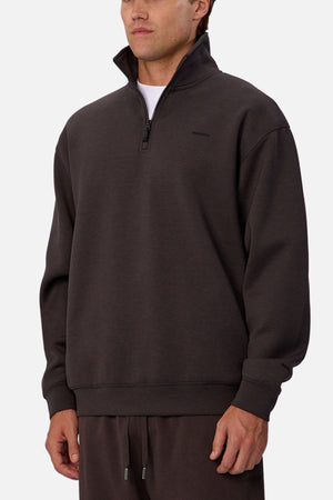 A man wears the Industrie The Tech Staunton Track Top, a dark brown athletic pullover with a high collar, paired with matching drawstring pants, standing against a plain white background.