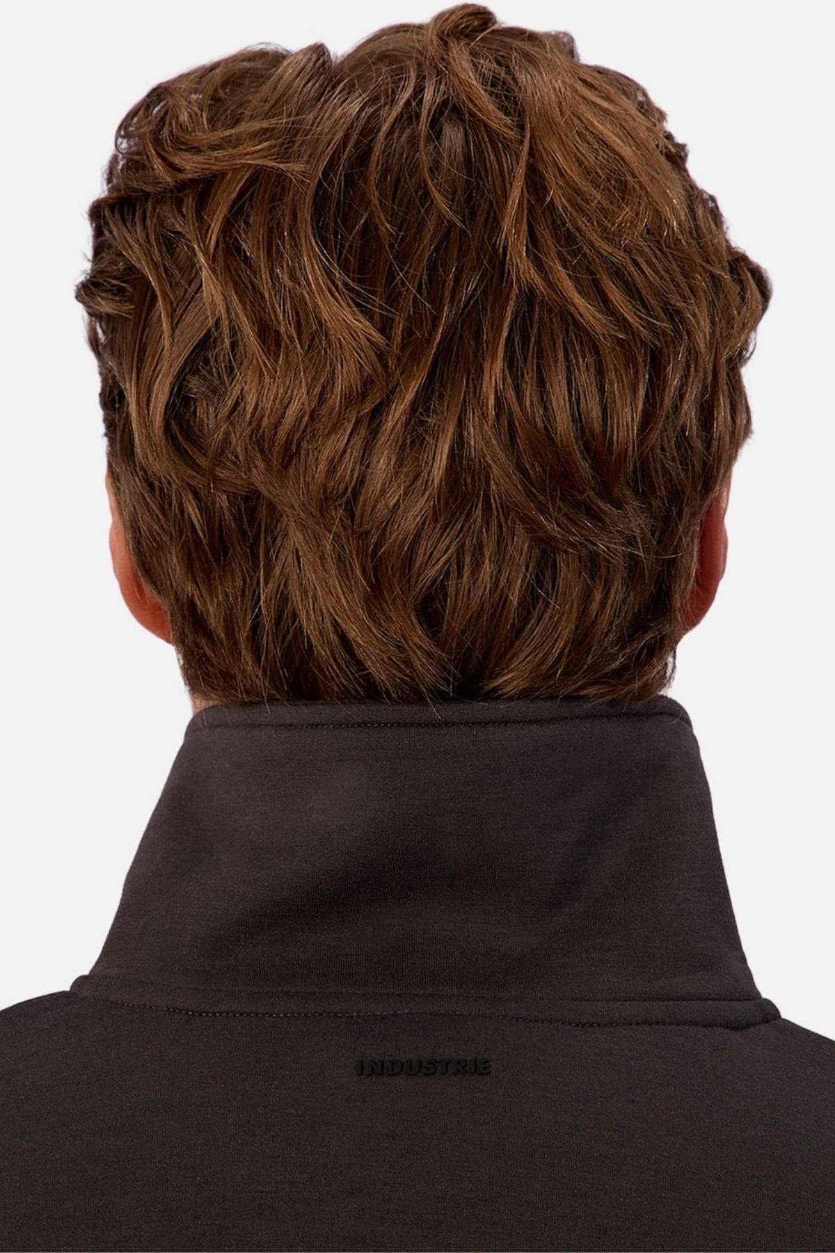 A person with wavy light brown hair is seen from behind, wearing the Industrie The Tech Staunton Track Top, a dark activewear jacket with a high collar featuring the "INDUSTRIE" brand name.
