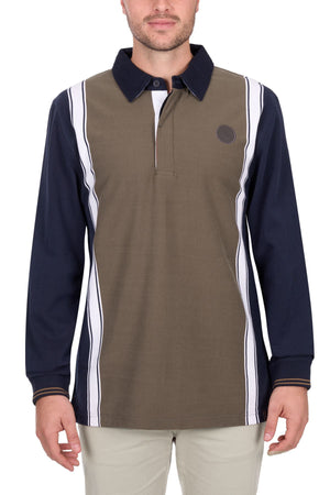 A man wears the Thomas Cook Travis Rugby: a long-sleeve polo with an olive-green front, navy sleeves, white vertical stripes, black collar, circular black chest logo, paired with light-colored pants.