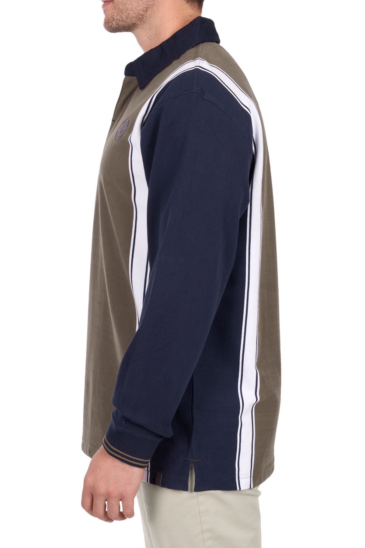 A man is seen from the side wearing the Thomas Cook Travis Rugby, a long-sleeve shirt with navy blue, olive green, and white vertical panels, paired with light-colored pants. His face is partially out of frame.