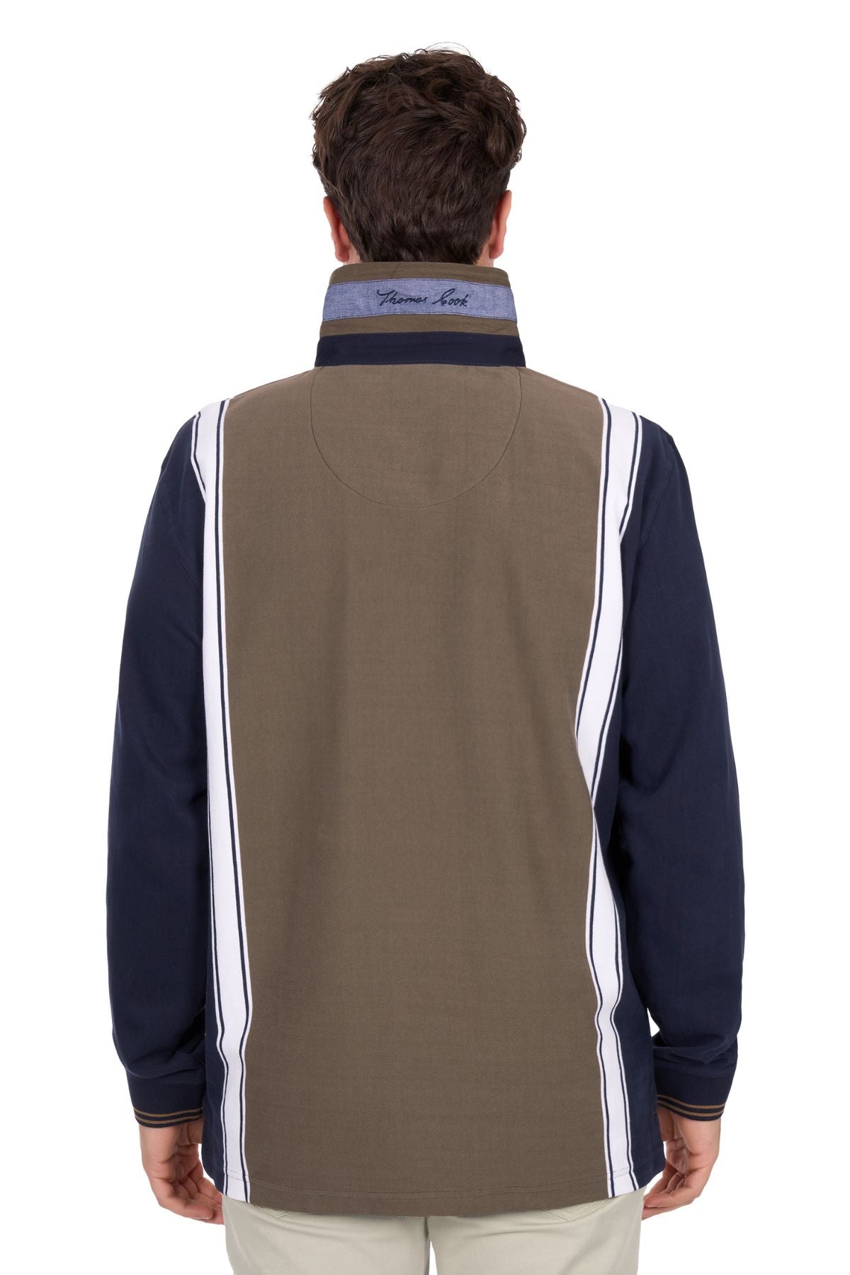 A man stands with his back to the camera, wearing the Thomas Cook Travis Rugby—a long-sleeve collared shirt with navy sleeves, olive and white vertical stripes on the back—and light-colored pants.