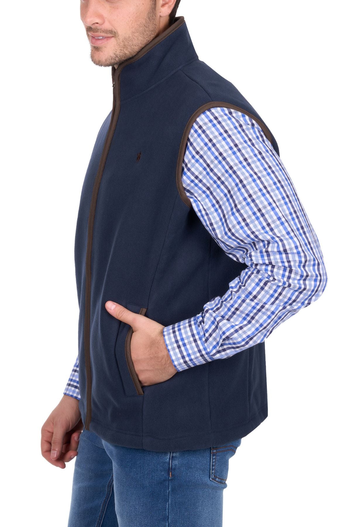 A man stands against a white background wearing the Thomas Cook Adrian Vest over a blue and white plaid shirt with blue jeans, one hand in his vest pocket.