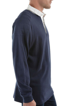 A side view of a man wearing the Thomas Cook Bill Rugby, a navy cotton jersey pullover styled like a classic rugby shirt, layered over a white collared shirt, set against a plain white background.