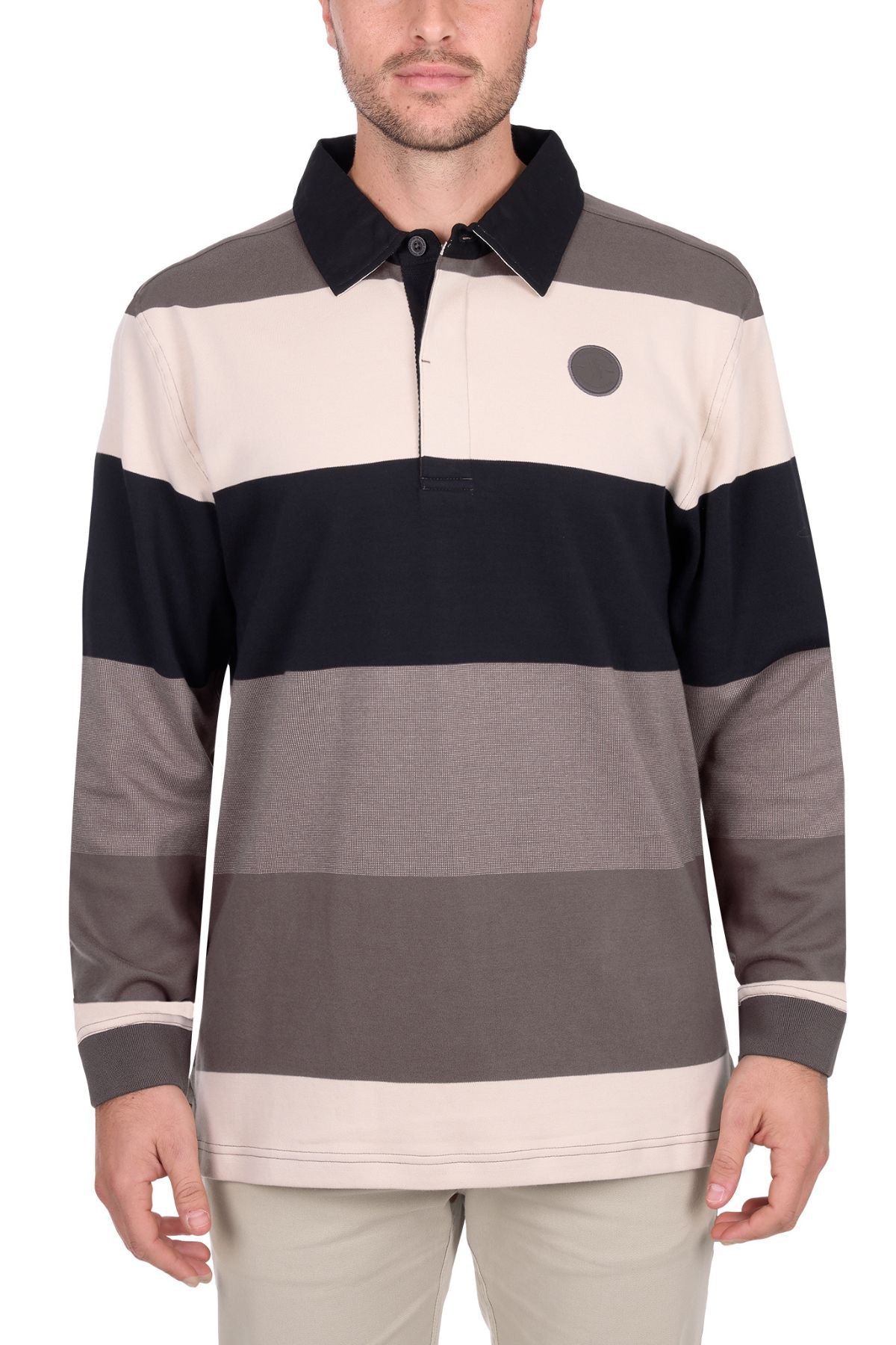 A man wears the Thomas Cook Brandon Rugby, a long-sleeve shirt with beige, black, gray, and brown horizontal stripes, a collar, and a small dark circle logo on the left chest. He stands against a white background.