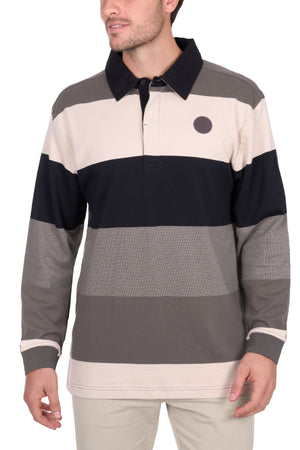 A man wears the Thomas Cook Brandon Rugby, a long-sleeve shirt with wide beige, black, and gray stripes, a collar, small circular chest patch, and light-colored pants.