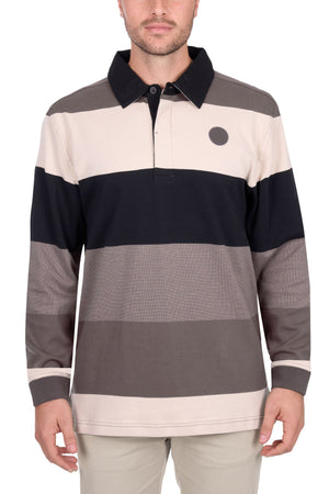 A man wears the Thomas Cook Brandon Rugby, a long-sleeve shirt with beige, black, gray, and brown horizontal stripes, a collar, and a small dark circle logo on the left chest. He stands against a white background.