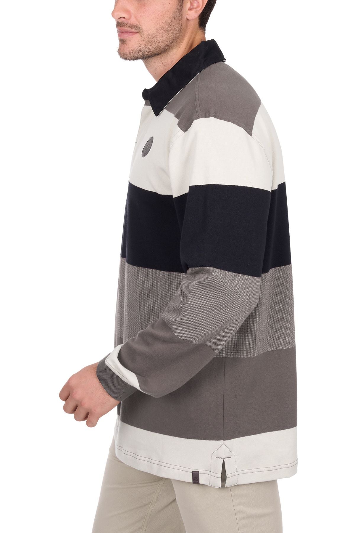 A man wears the Thomas Cook Brandon Rugby, a long-sleeve striped shirt in white, gray, and black tones, paired with beige pants as he walks forward against a white background, his head slightly turned and face partially visible.