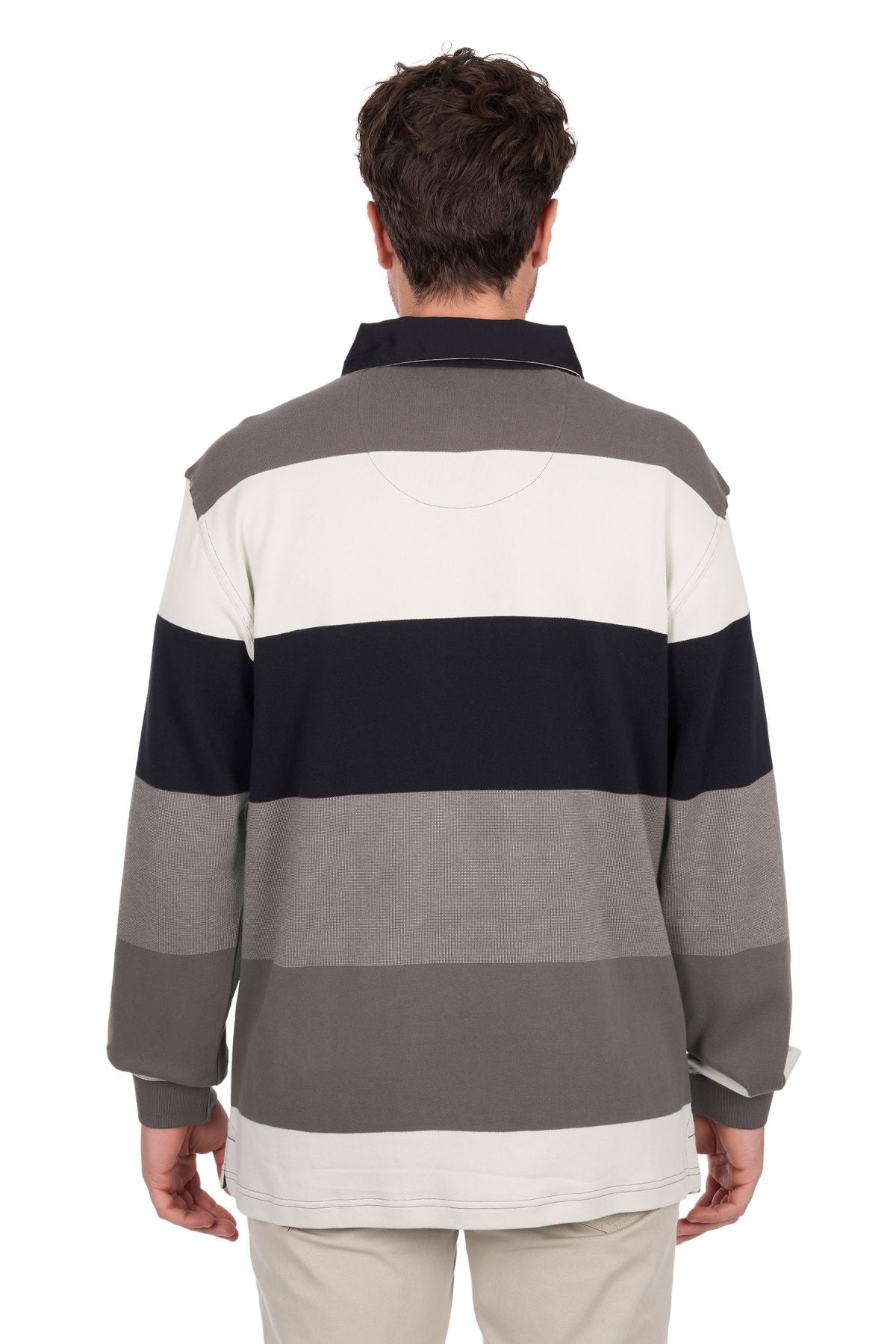A man with short brown hair faces away from the camera, wearing the Thomas Cook Brandon Rugby—a long-sleeve polo shirt featuring wide horizontal stripes in gray, black, and cream—paired with light-colored pants.