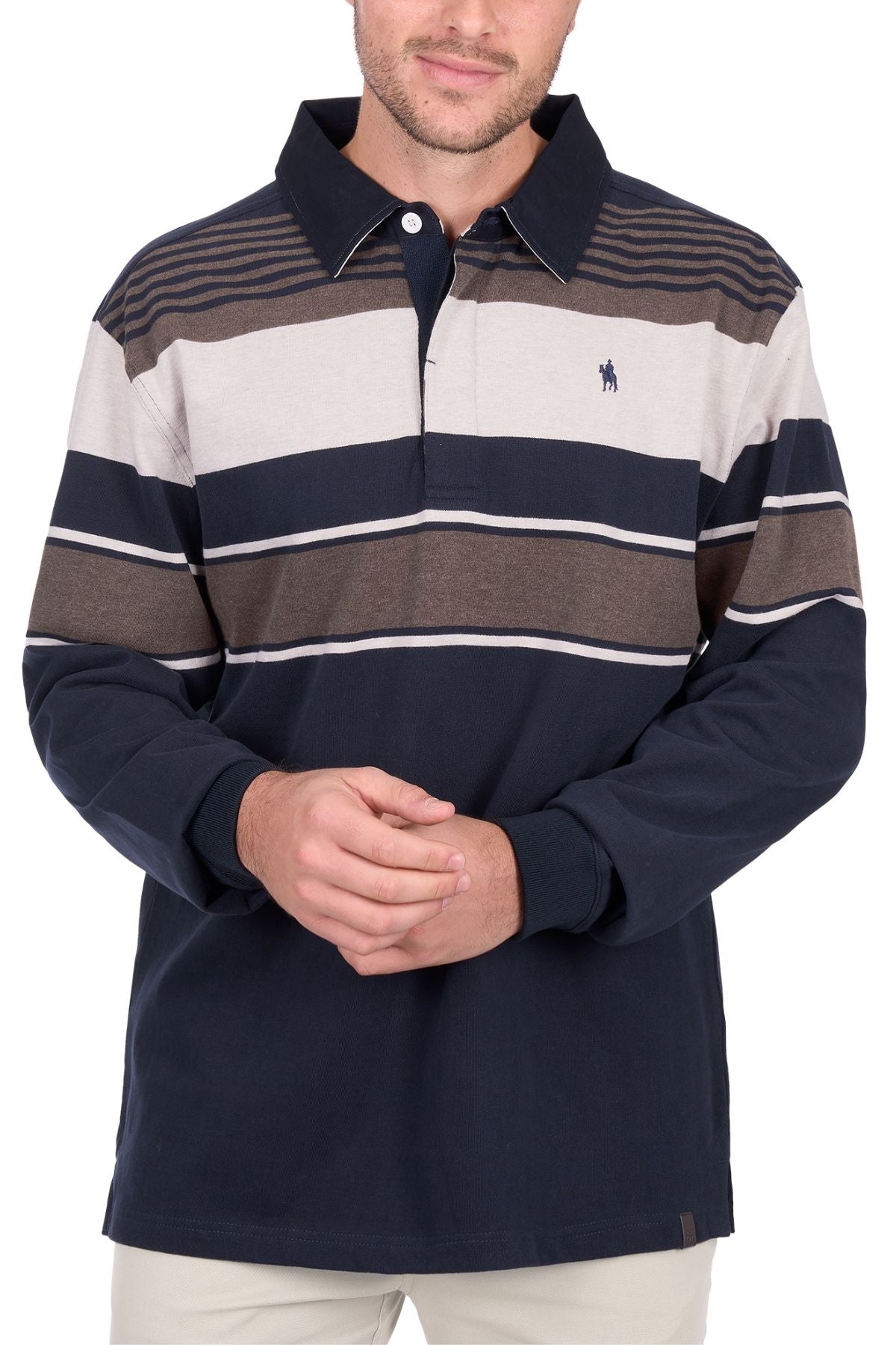 A man stands with his hands clasped, wearing the Thomas Cook Bryan Stripe Rugby—a navy, beige, and brown striped long-sleeve polo shirt with a collar—paired with light pants.