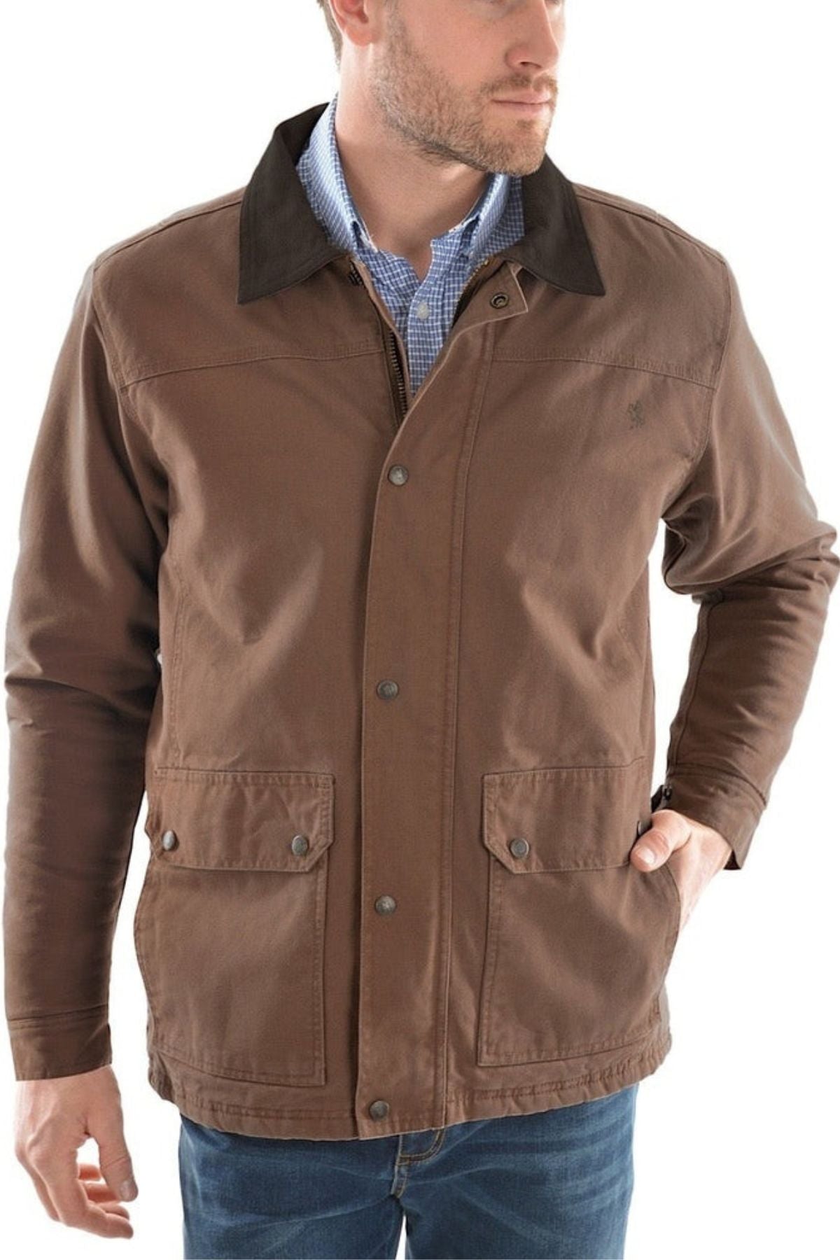A man wearing the Thomas Cook Canvas Jacket—brown with front pockets and a leather collar—over a blue checked shirt, stands with one hand in his pocket.