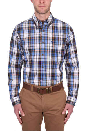 A man wears the Thomas Cook Daniel Shirt, a blue, brown, and white yarn-dyed check long-sleeve shirt tucked into tan pants with a brown belt, standing against a white background.