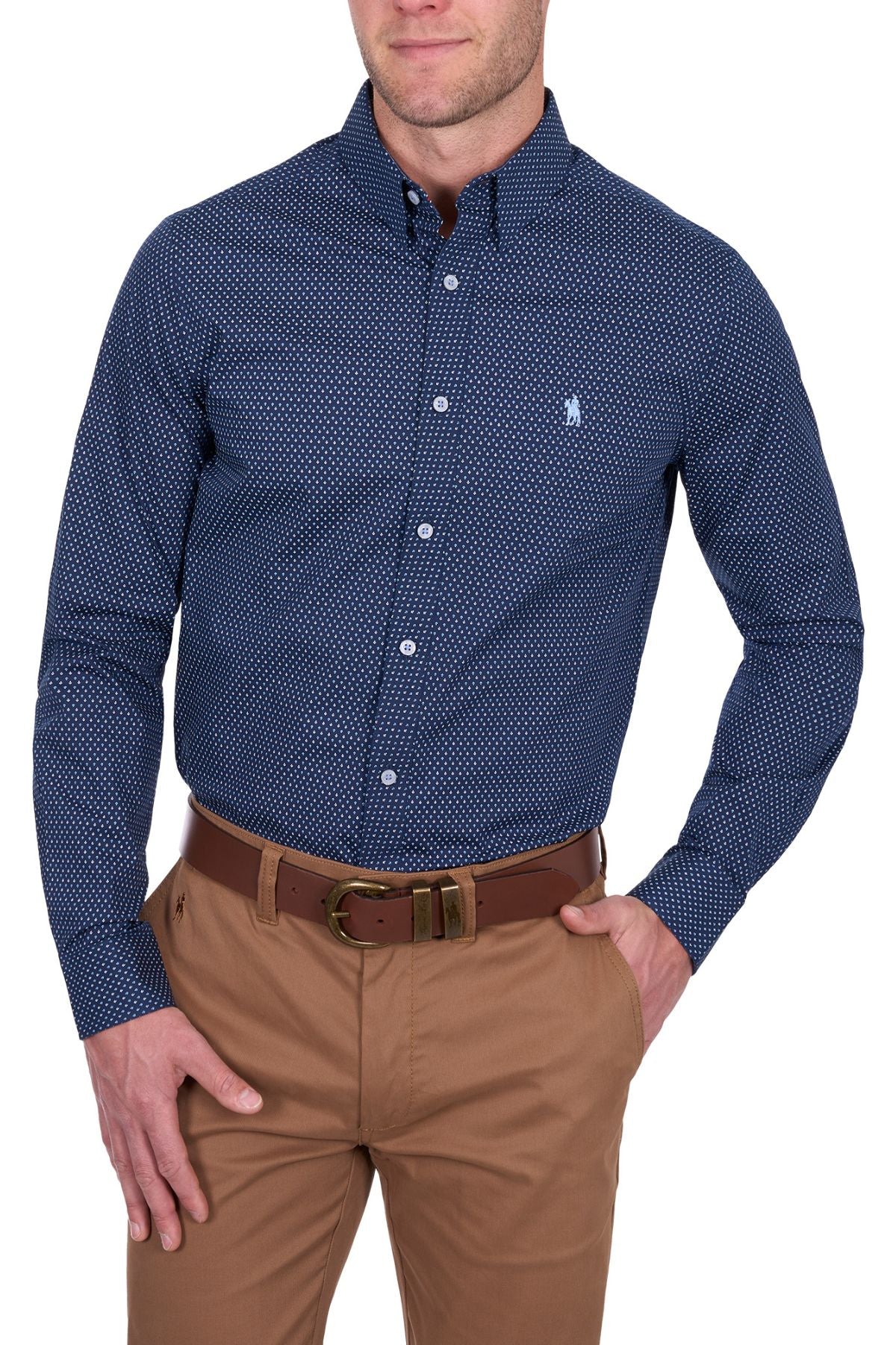 A man wears the Thomas Cook David Tailored Shirt, featuring a dark blue geometric print and small chest logo, tucked into light brown pants with a brown belt.