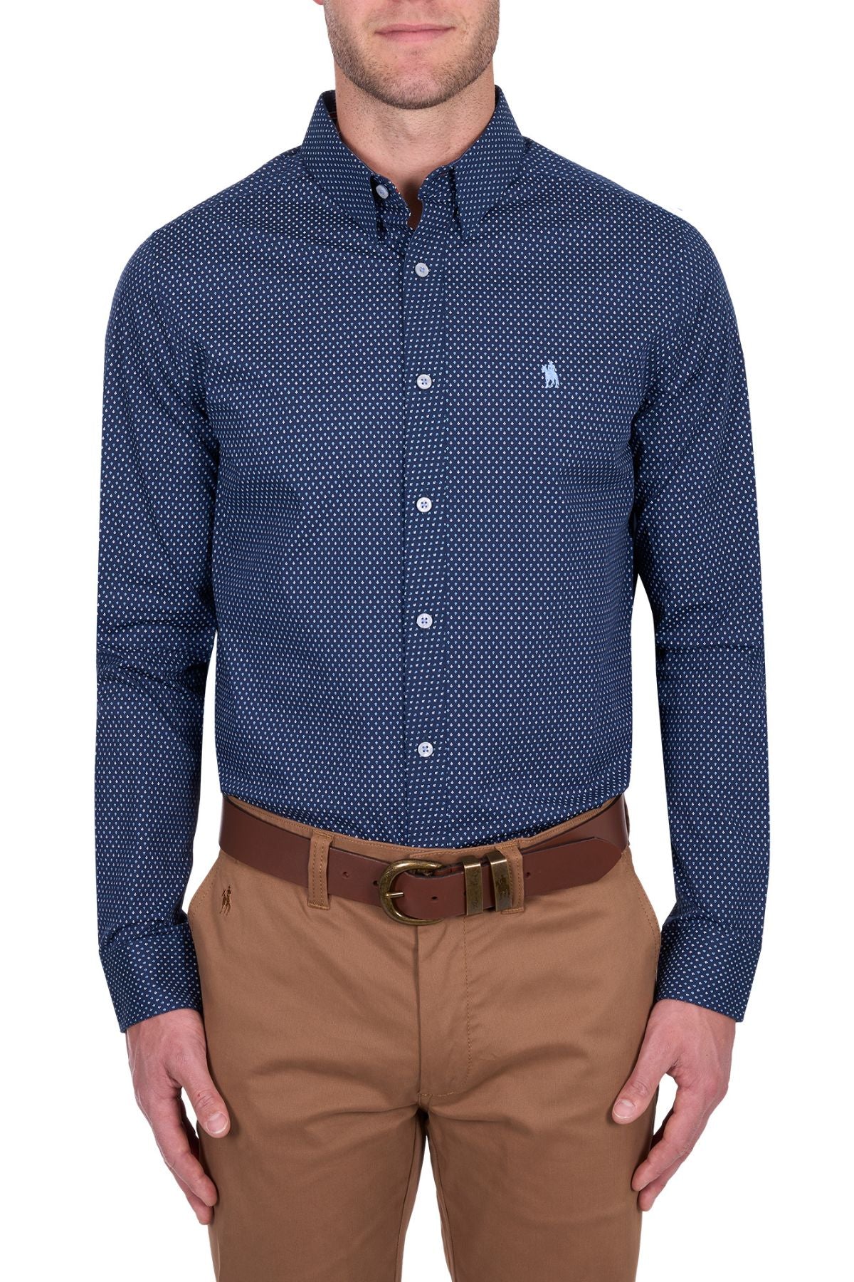 A man wears the Thomas Cook David Tailored Shirt, a navy blue geometric print, long-sleeve button-down, paired with khaki pants and a brown belt, standing against a plain white background.