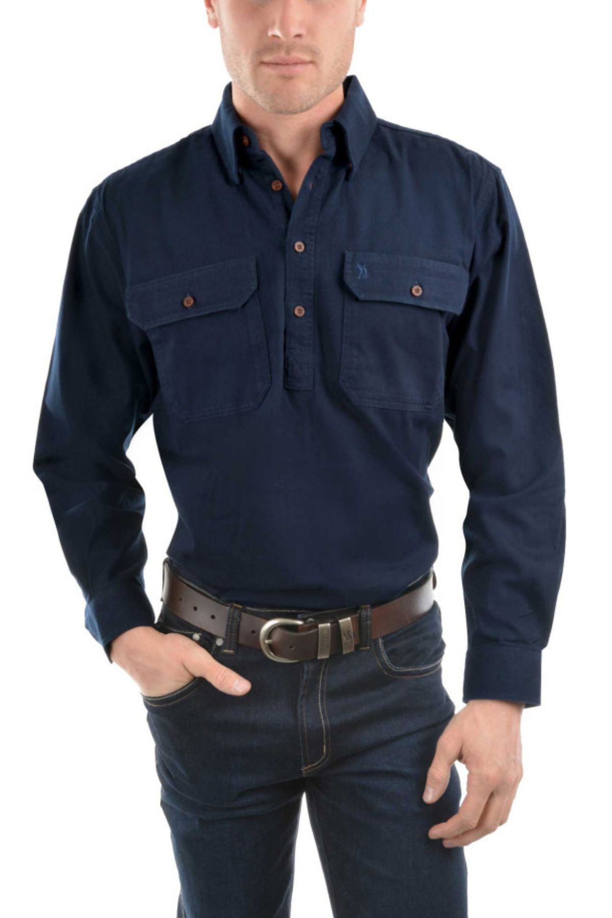 A man stands with one hand in his pocket, wearing the Thomas Cook Heavy Drill Half Placket Shirt in dark blue, paired with dark jeans and a black belt with a silver buckle.