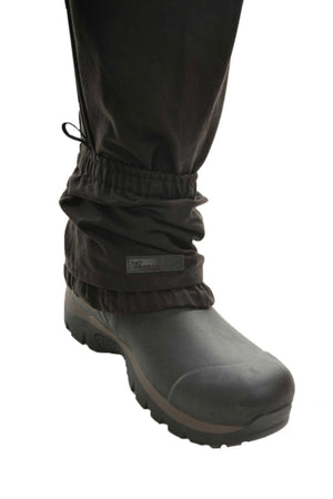 A close-up of a person’s lower leg wearing Thomas Cook High Country Bushman Short Oilskin Gaiters over black pants and sturdy hiking boots for outdoor protection, isolated on a white background.