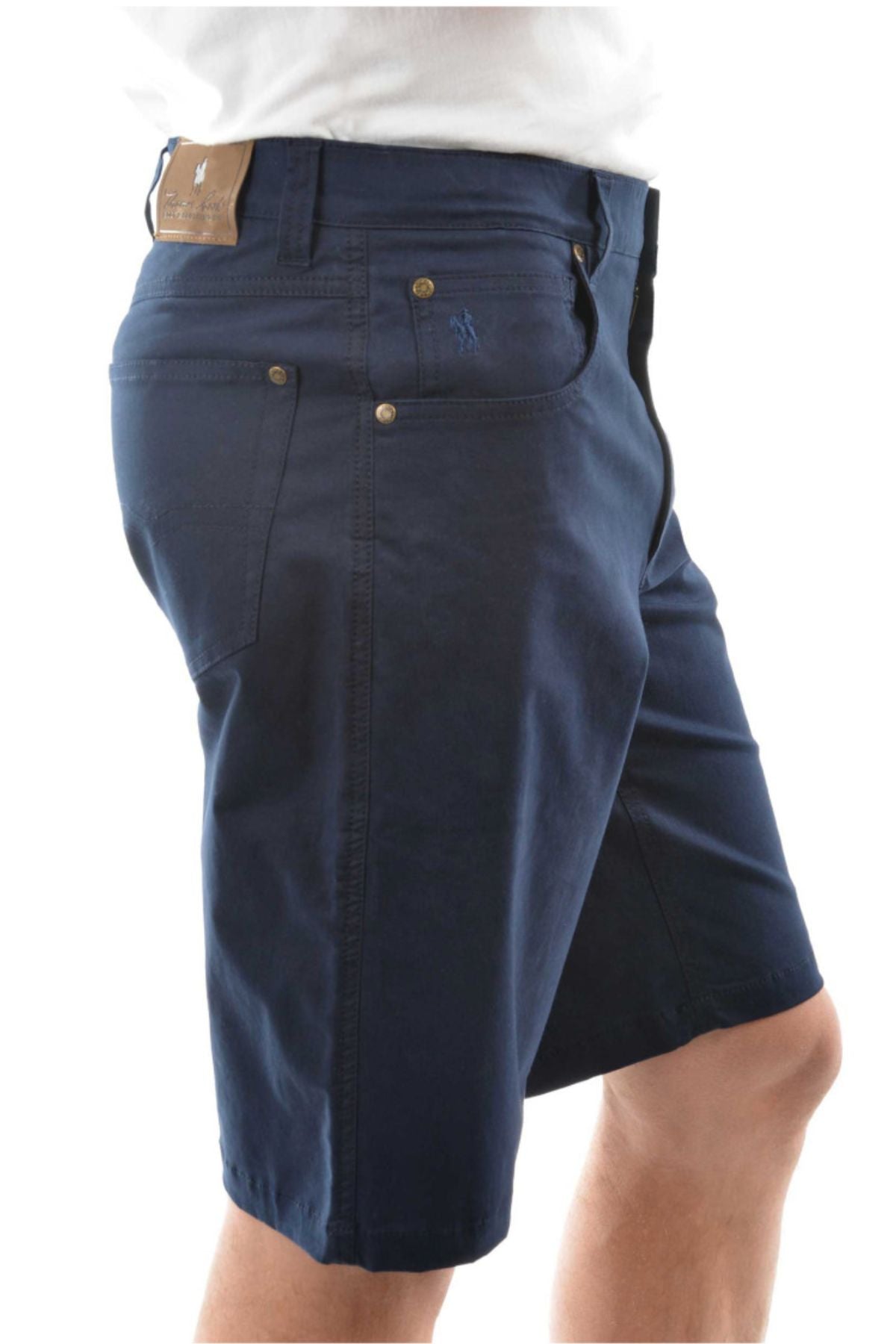 A person shown from the side wears a white shirt and navy Thomas Cook Jake Comfort Waist Shorts, featuring knee-length fit, pockets, a leather patch, and a small embroidered logo on the back pocket.