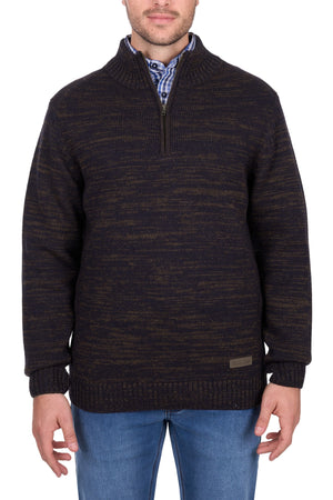 A man wearing the Thomas Cook Jesse 1/4 Zip Jumper, a dark brown and black marled heavyweight wool sweater, over a plaid shirt with blue jeans, stands against a white background.