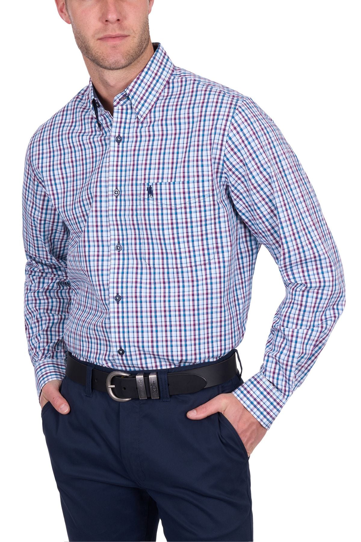 A man wears the Thomas Cook Joseph Shirt, a long-sleeved, button-up plaid made from 100% cotton in blue, white, and red. It’s tucked into navy pants with a black belt; his hands are in his pockets and his face is partially out of frame.