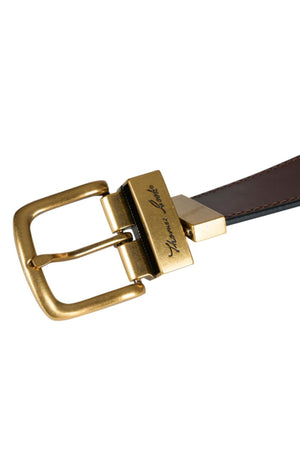 A close-up of the Thomas Cook Lincoln Reversible Belt, crafted from genuine leather, featuring a shiny gold rectangular buckle and a matching engraved gold clasp.
