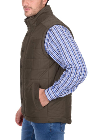 A man stands in side profile with one hand in his pocket, wearing the Thomas Cook Matt Vest—a brown, quilted, lined vest—over a blue and white plaid shirt and blue jeans.